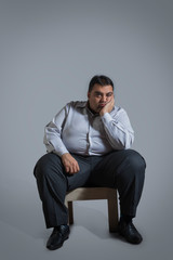 Overweight man sitting on chair in sad mood with chin resting on hand