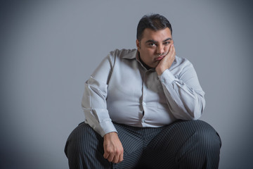 Obese man sitting in sad mood with chin resting on hand