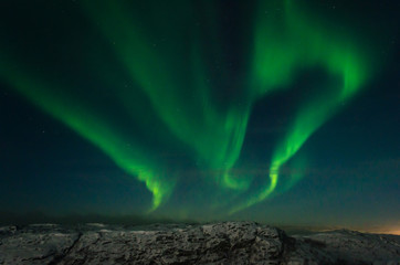 Northern lights, aurora in the night sky above the snowy hills.