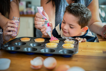 Mother helping son to put frosting onto cupcakes