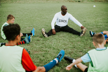 Football coach stretching with junior players