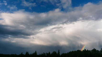 dramatic sky with dark and light clouds with a rainbow over the forest