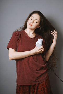 young brunette woman blow-drying her long hair with blow dryer or drier at home