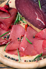 Sliced bresaola with a sprig of rosemary and red pepper on a wooden board