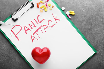 Clipboard with text PANIC ATTACK, heart and scattered pills on grey background