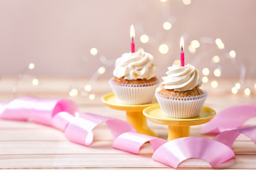 Delicious birthday cupcakes with burning candles on wooden table  against blurred lights