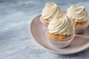 Plate with delicious cupcakes on grey table