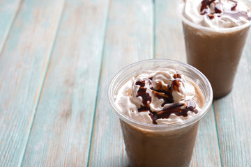 Cold coffee covered with whipped cream and chocolate in wet plastic cup on wooden table