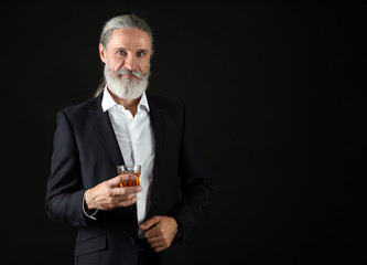 Elderly businessman with glass of whiskey on dark background