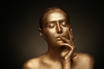 Beautiful young woman with golden paint on her body against dark background