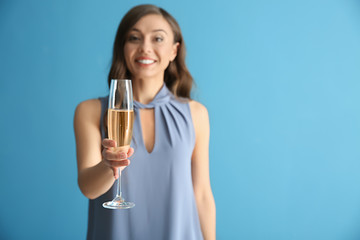 Beautiful young woman with glass of champagne on color background