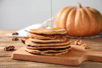 Pouring of sweet honey onto hot pumpkin pancakes on wooden board