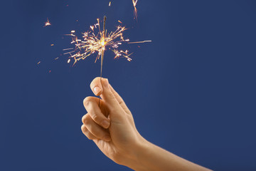 Female hand with Christmas sparkler on color background