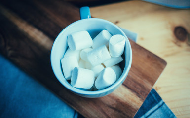 Fluffy white marshmallow in blue round mug on old wooden table