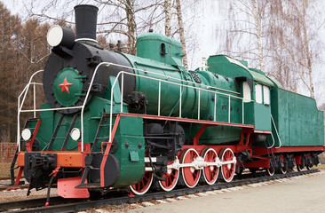 Obraz premium Side view of classic old green soviet steam locomotive with red star on rail tracks