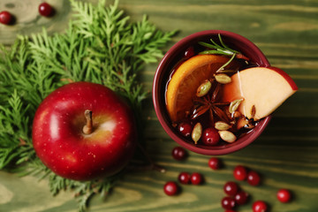 Cup of tasty mulled wine and apple on wooden background