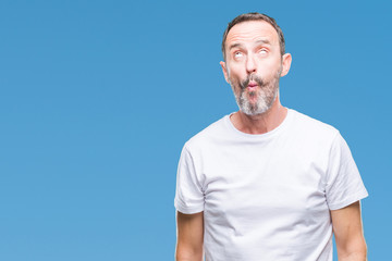 Middle age hoary senior man wearing white t-shirt over isolated background making fish face with lips, crazy and comical gesture. Funny expression.