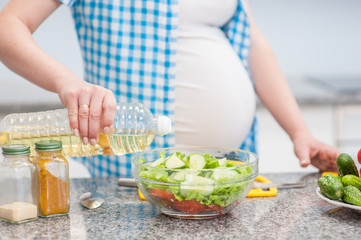 Obraz na płótnie Canvas Close up pregnant woman in kitchen making a salad