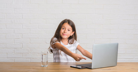 Young hispanic kid sitting on the table using computer laptop very happy pointing with hand and finger