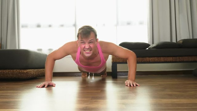 Playful handsome guy in a pink t-shirt engaged in fitness, in the living room of his house.