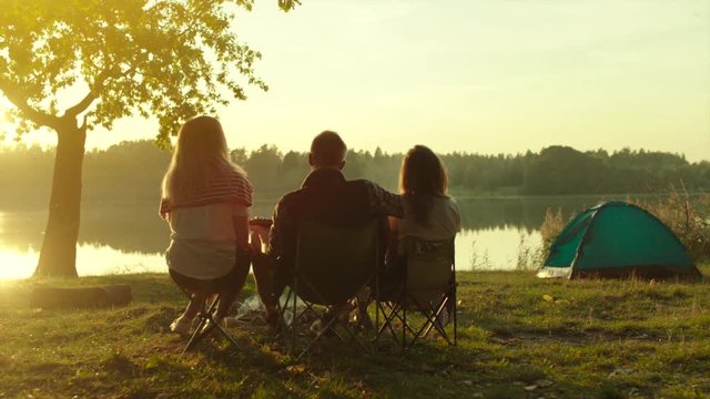 Backshot of friends enjoying sunset at the lake on camping with tents