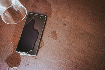 Smartphone wet by accident on wooden table. Glass of water spilled.