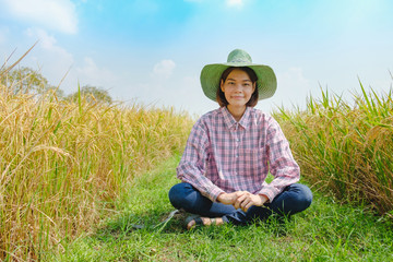 Naklejka na ściany i meble Portrait Smile farmer woman wear hat sitting with beautiful rice paddy in rice field Thailand.