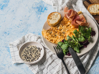 Omelette or scramble with sesame, corn lettuce, prosciutto on white plate on a blue background © senteliaolga