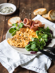Omelette or scramble with sesame, corn lettuce, prosciutto on white plate and croutons on wood background