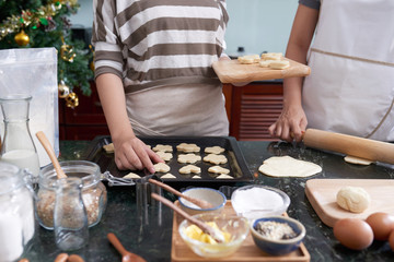 Teenage girl putting cookies on metal tra for baking