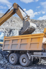 The process of loading a truck with an excavator on a blue sky background