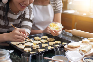 Smiling teenage girl enjoying applying soft butter on Christmas cookies