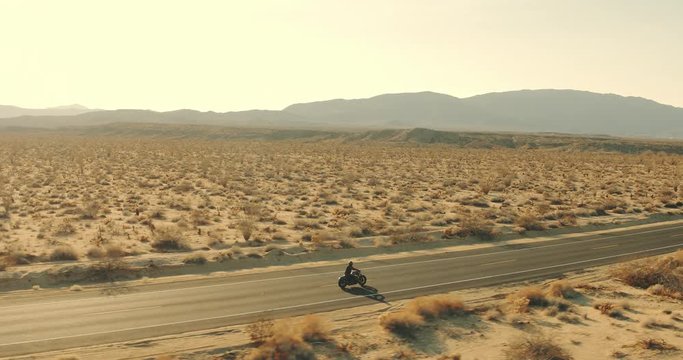 Aerial view of man riding motorcycle down desert road at sunset 