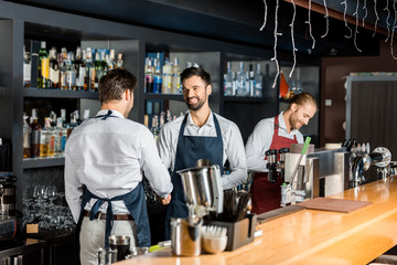 adult barmen in aprons shaking hands near counter