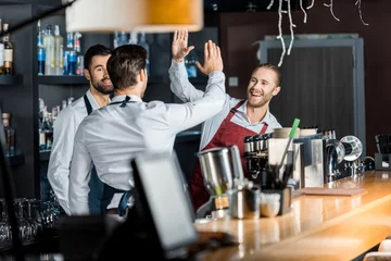 Zelfklevend Fotobehang Handsome smiling barmen in aprons high five at workplace © LIGHTFIELD STUDIOS