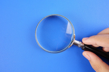 Hand holding magnify glass over a blue background