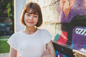 Beautiful asian woman looking at the camera while standing on a Street Art Graffiti wall background
