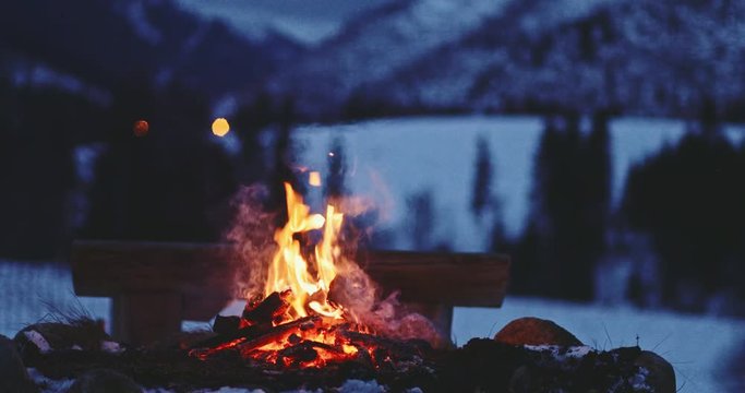 Burning Bonfire With Winter Mountains in Background. SLOW MOTION. Fairytale snow covered view with campfire burning outdoors at dusk. 