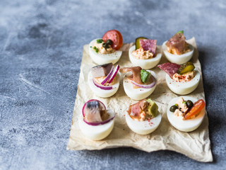 Stuffed eggs with various topping. Prosciutto, herring, pickled cucumber, sausage, radish, tomato, capers and sesame on boiled egg halves.
