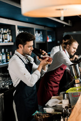 adult barman in apron shaking cocktail in glass with shaker