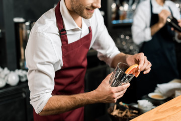 cropped view of smiling barman decorating glass with grapefruit slice