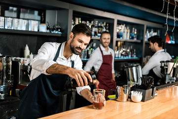 smiling bartender pouring cocktail in glass at wooden counter