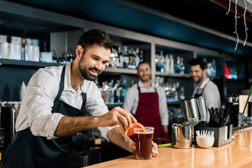 cheerful bartender decorating cocktail at wooden counter