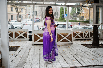 Indian hindu girl at traditional violet saree posed at street against wooden terrace.