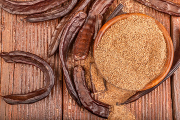 Carob pods and carob powder in a bowl on rustic background