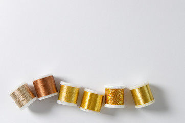 Golden thread coils on white background, sewing, copy space. Top view