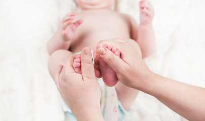 Mother doctor massage therapist doing heel massage for a happy child, applies oil on her leg, on a white background