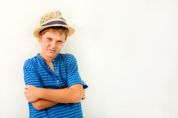 Tanned boy - teenager in a straw hat and blue shirt against a white wall.