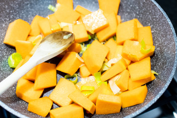 Pumpkin and leek cubes are cooked and sautéed in a non-stick pan on the stove. Cook a recipe with pumpkin and leek, pour the pumpkin into the pan