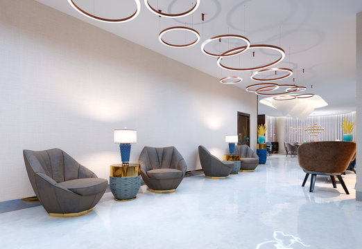 A Modern Hotel With A Reception Area And Lounge With Large Upholstered Designer Chairs And A Large Chandelier Of Golden Rings.